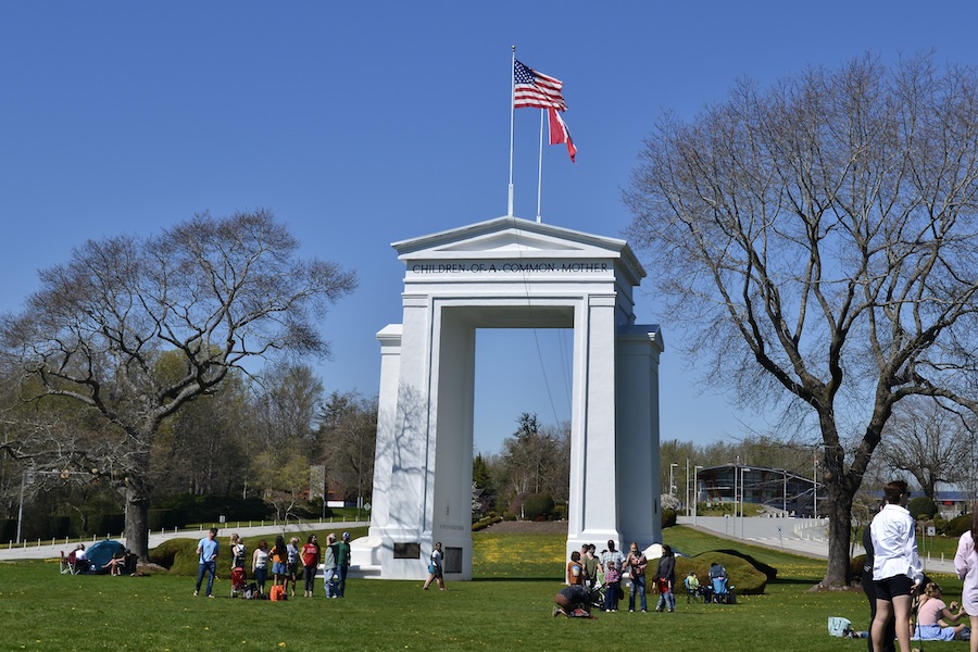 The Peace Arch as seen from the American side with groups of people visiting in the spring time and a tent set up to one side. Photography by Rhonda Jesckey