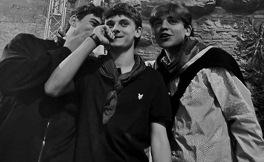 Three young men telling secrets at a public outdoor gathering. Photography by Rhonda Jesckey.