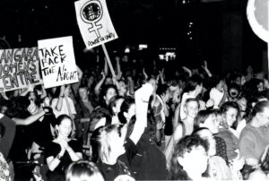 A big crowd of women fill Robson Street in Vancouver carrying signs that say - Take Back the Night, Power in Unity and Langara Women's Centre. Photography by Rhonda Jesckey.